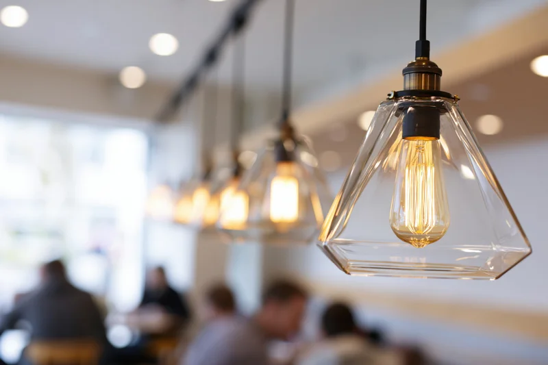 Row of geometric pyramid-shaped clear glass pendant lights hanging in a cafe interior with blurred diners below