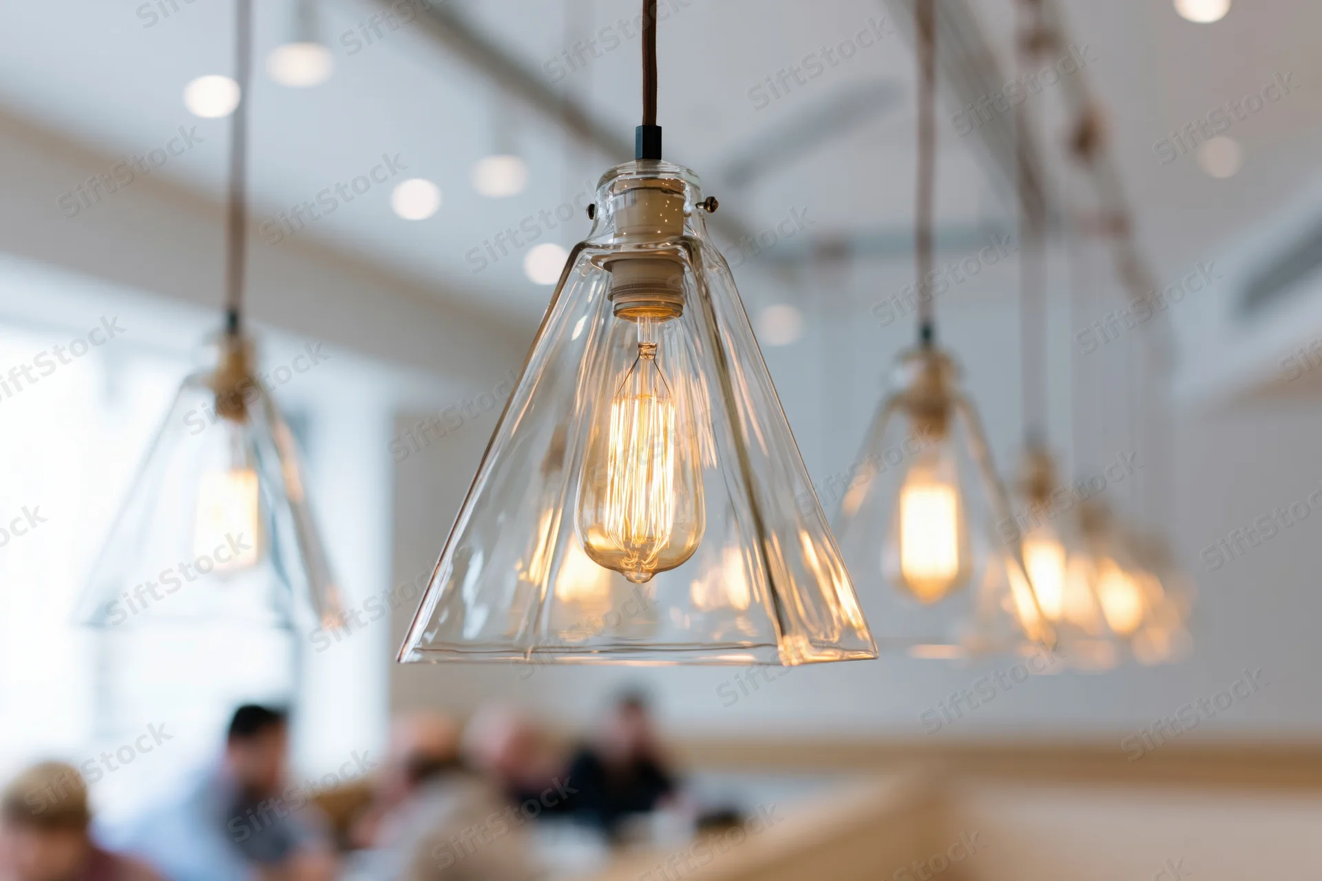 Row of geometric pyramid-shaped clear glass pendant lights hanging from ceiling in restaurant interior with warm glow