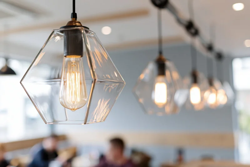 Row of geometric glass pendant lights hanging in a cafe interior with blurred diners below