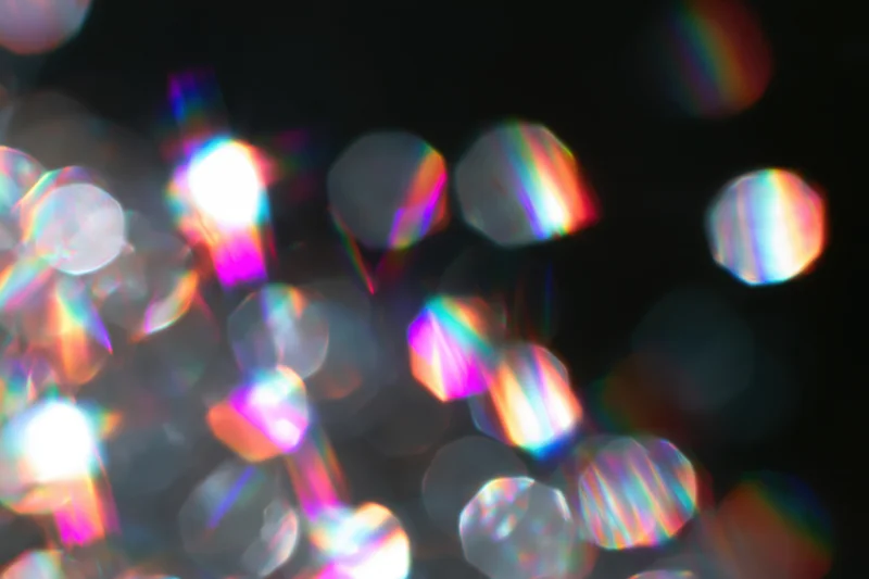 Scattered prismatic light refractions and bokeh circles float against a dark background