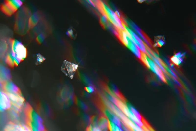 Scattered rainbow light refractions and prismatic lens flares across a dark surface with faceted crystals reflecting color