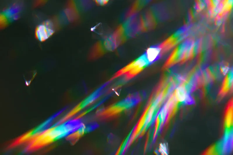 Scattered rainbow light refractions and prismatic lens flares across a dark surface