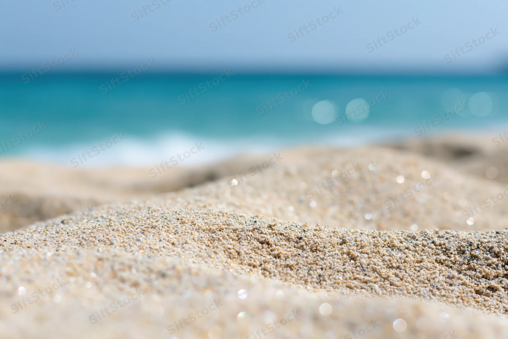 Close-up of pale golden beach sand with blurred ocean and sky in background