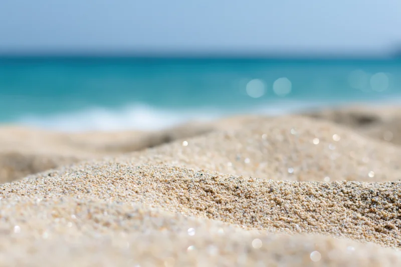 Close-up of pale golden beach sand with blurred ocean and sky in background