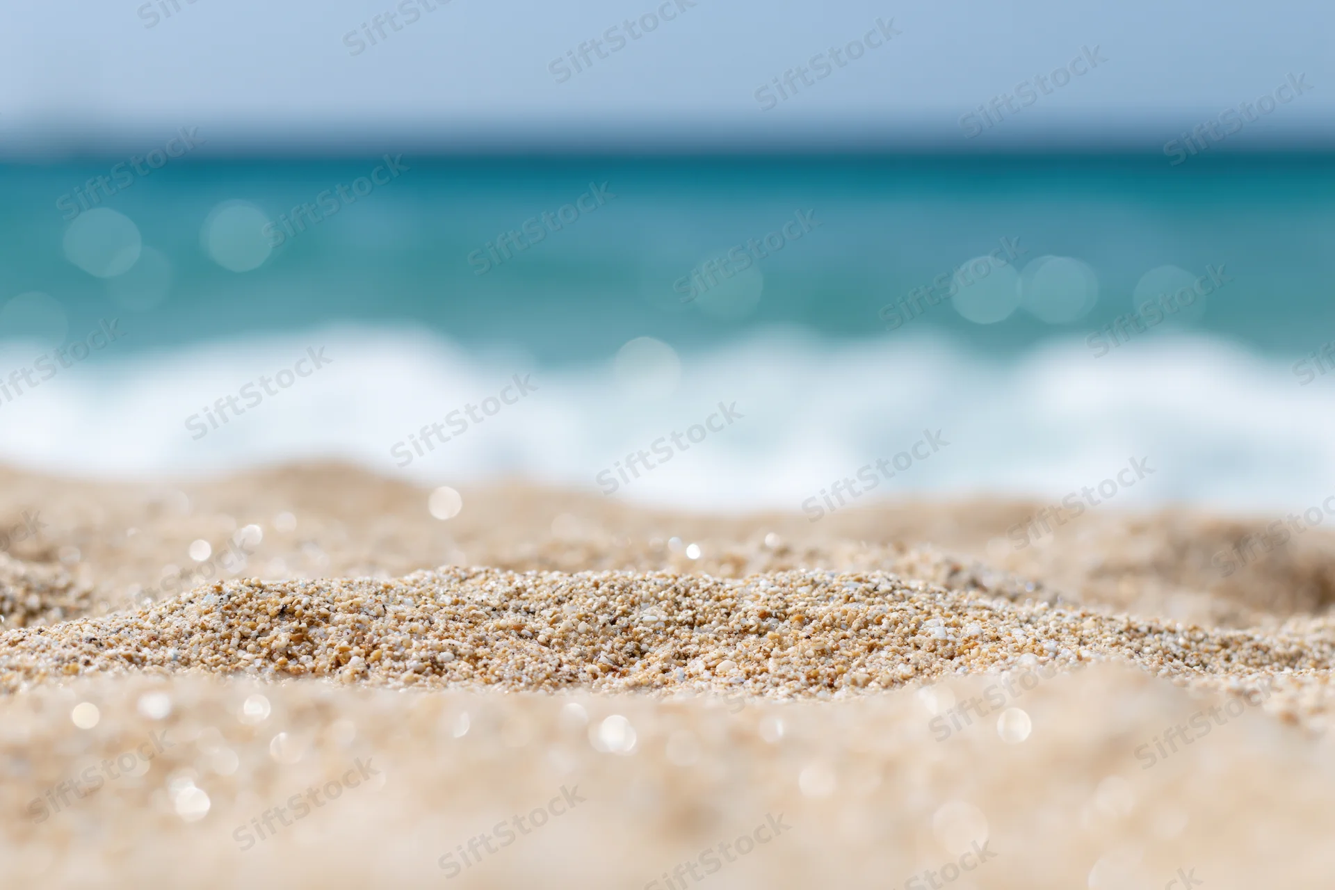 Close-up of pale golden beach sand with blurred ocean waves in the background