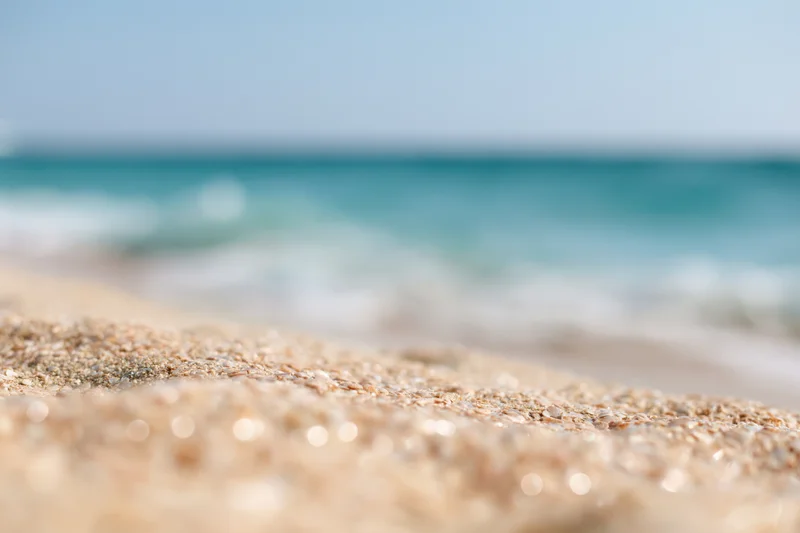 Closeup of golden beach sand in foreground with blurred ocean waves beyond