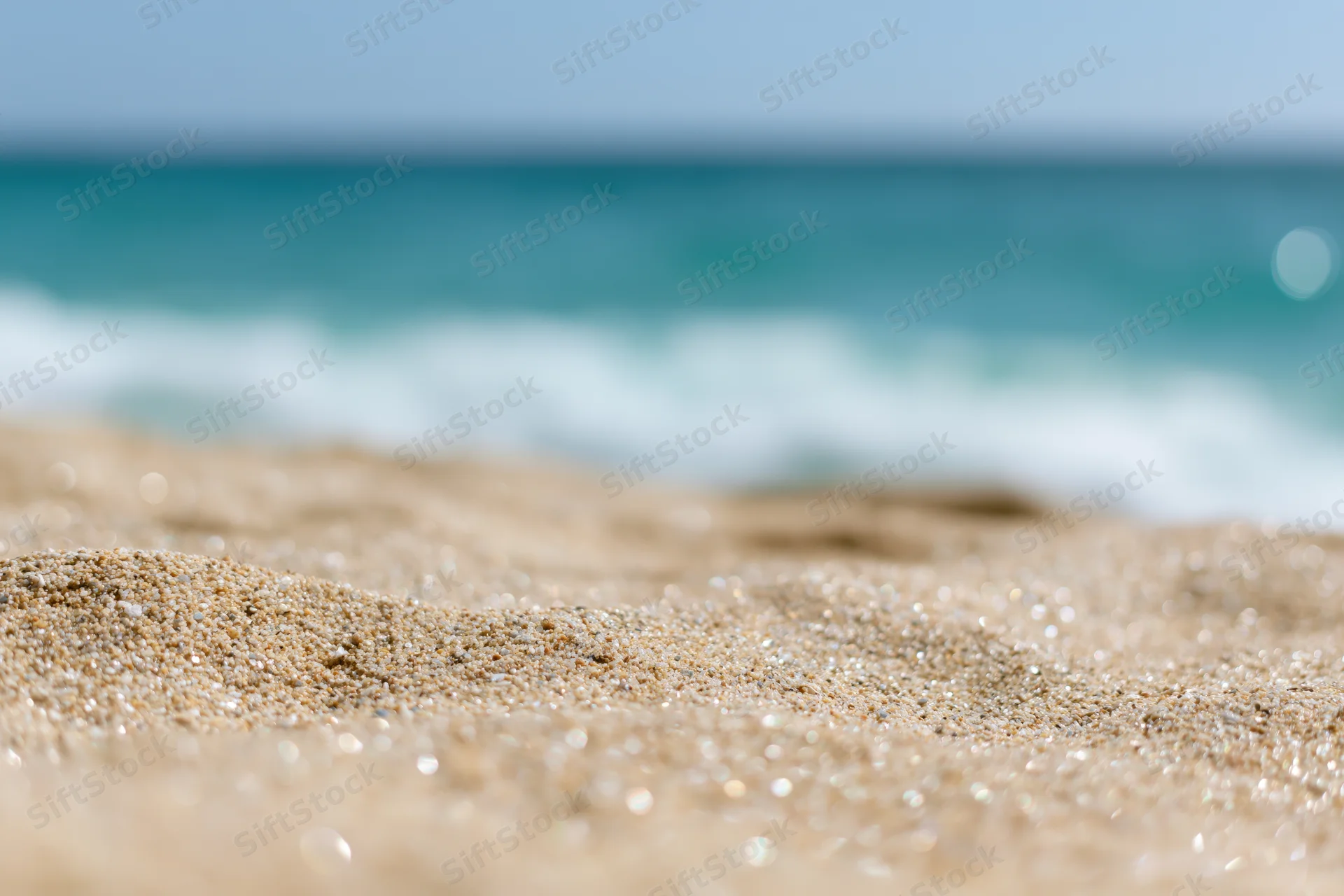 Close-up of pale golden beach sand with blurred ocean waves in the background