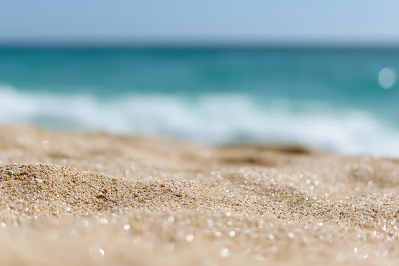 Close-up of pale golden beach sand with blurred ocean waves in the background