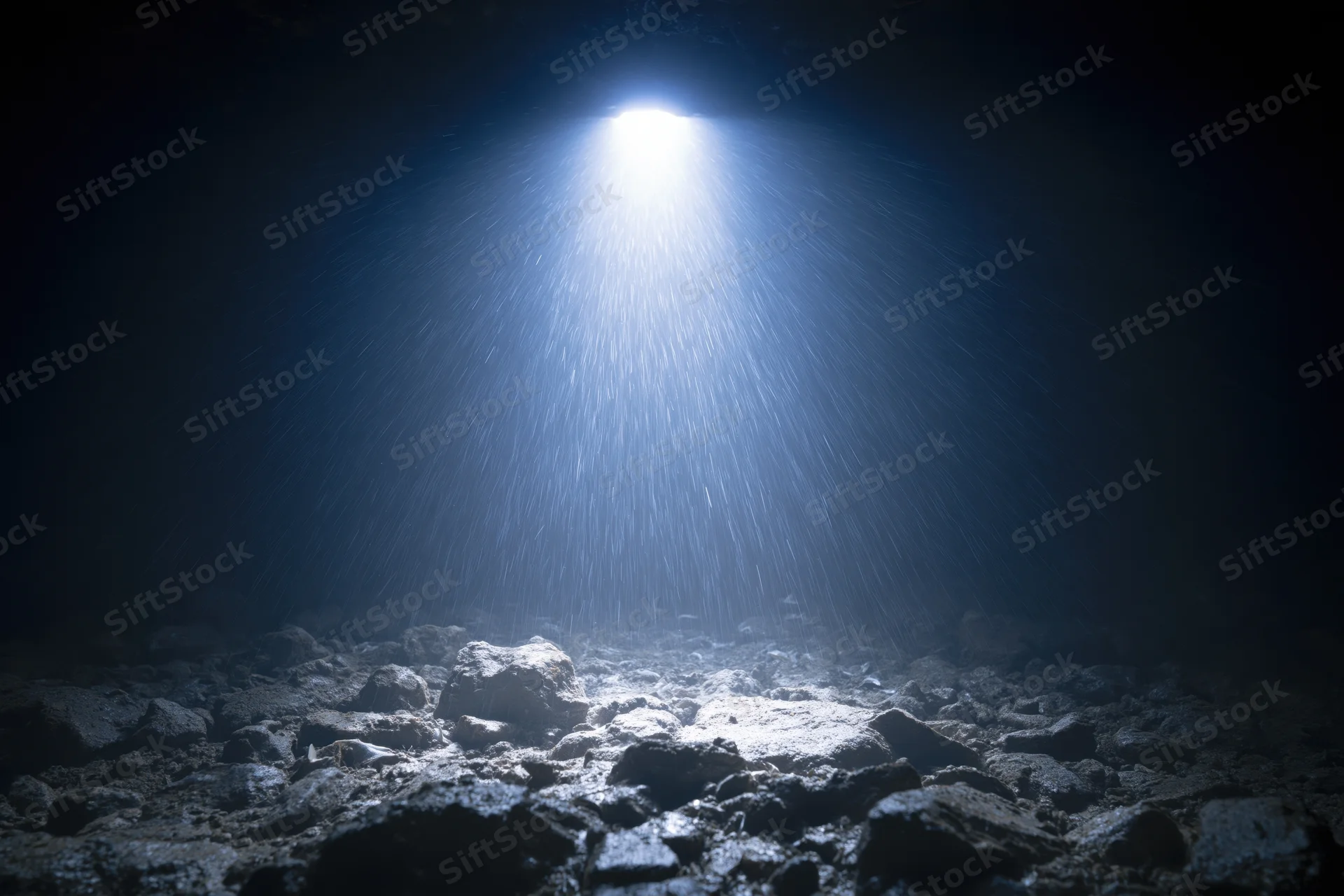 Bright light beam shining down onto rocky seabed in dark underwater cave