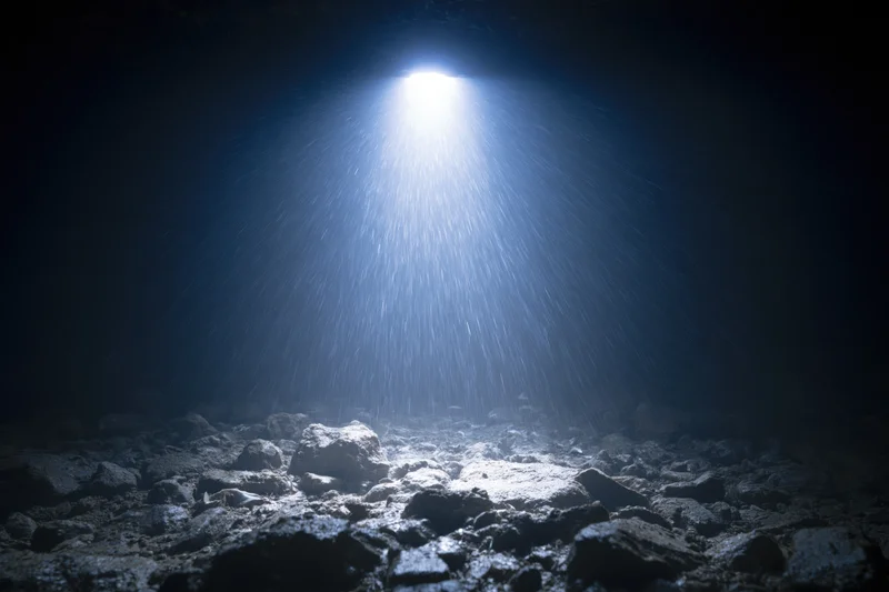 Bright light beam shining down onto rocky seabed in dark underwater cave