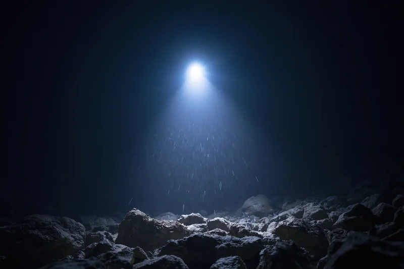 Bright light beam shining down through dark water onto rocky ocean floor