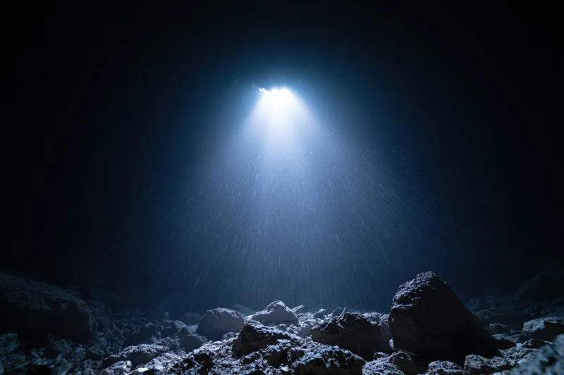 Bright light beam shining down into dark rocky cave interior