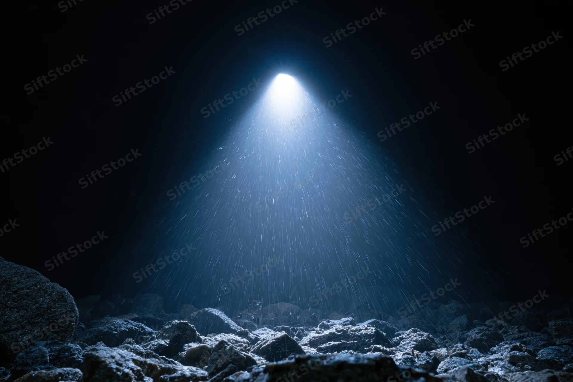 Bright light beam shining down through dark cave onto rocky ground