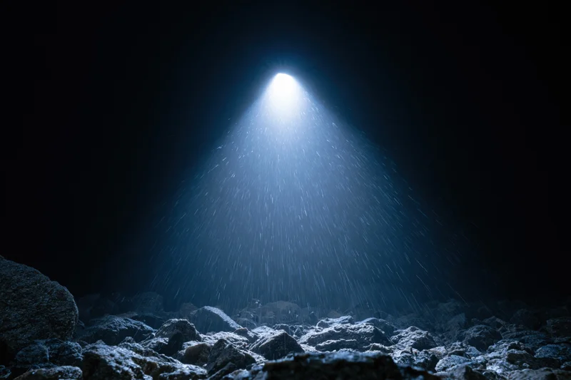 Bright light beam shining down through dark cave onto rocky ground