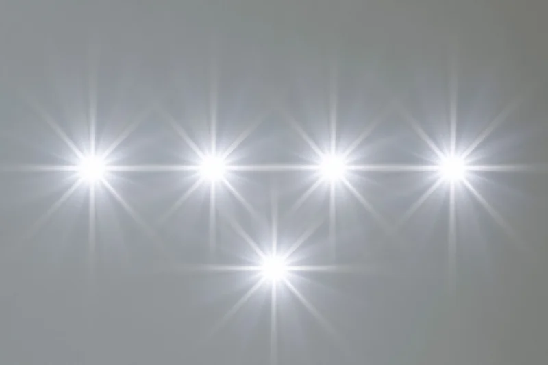 Six bright white lens flare star bursts arranged in two rows against a neutral gray background