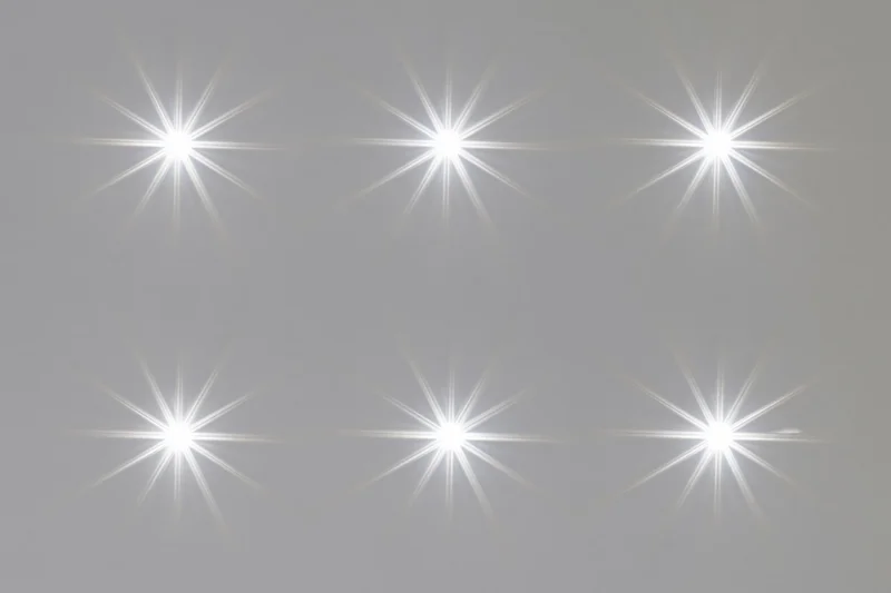 Six bright white lens flare star bursts arranged in two rows on a neutral gray background