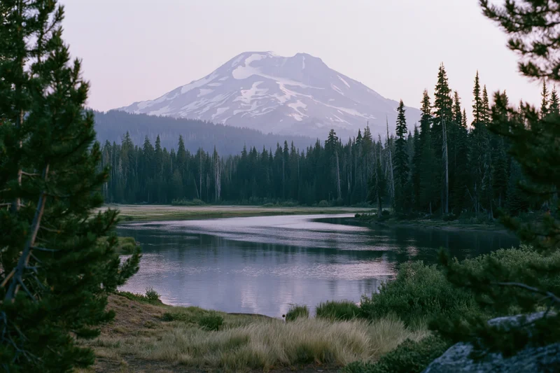 Snow-capped volcanic mountain reflected in calm alpine lake surrounded by pine forest at dusk