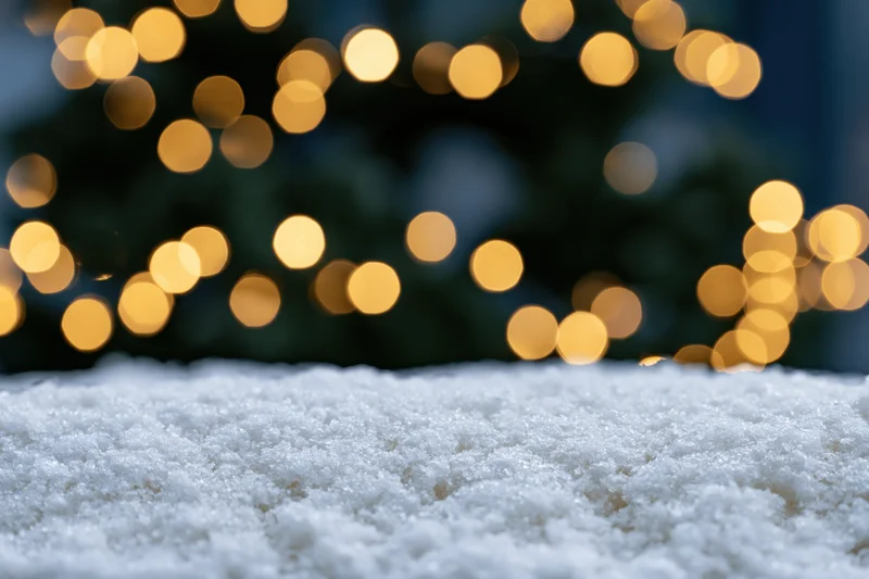 Snow-covered surface in foreground with blurred golden christmas lights in background