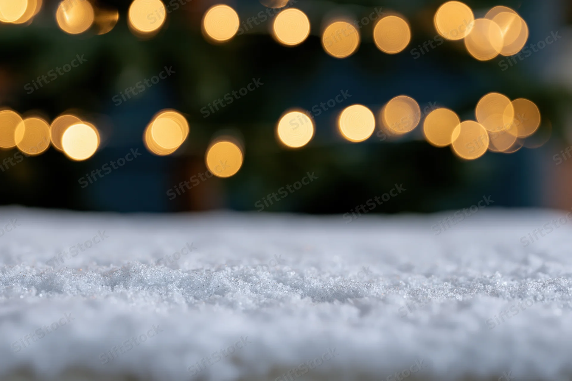 Snow-covered surface in foreground with blurred golden christmas lights in background