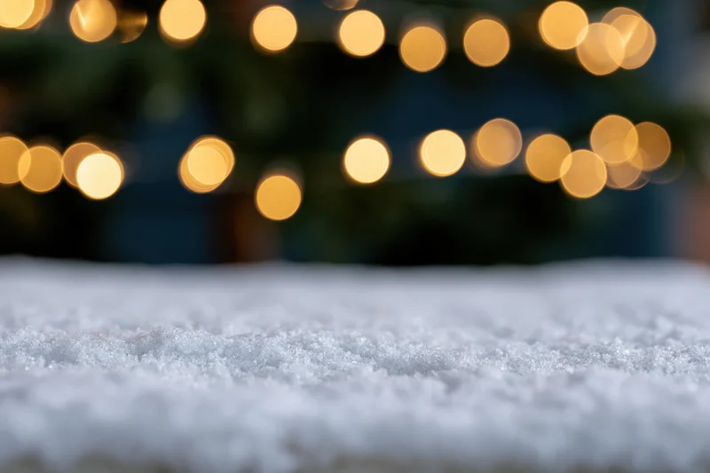 Snow-covered surface in foreground with blurred golden christmas lights in background