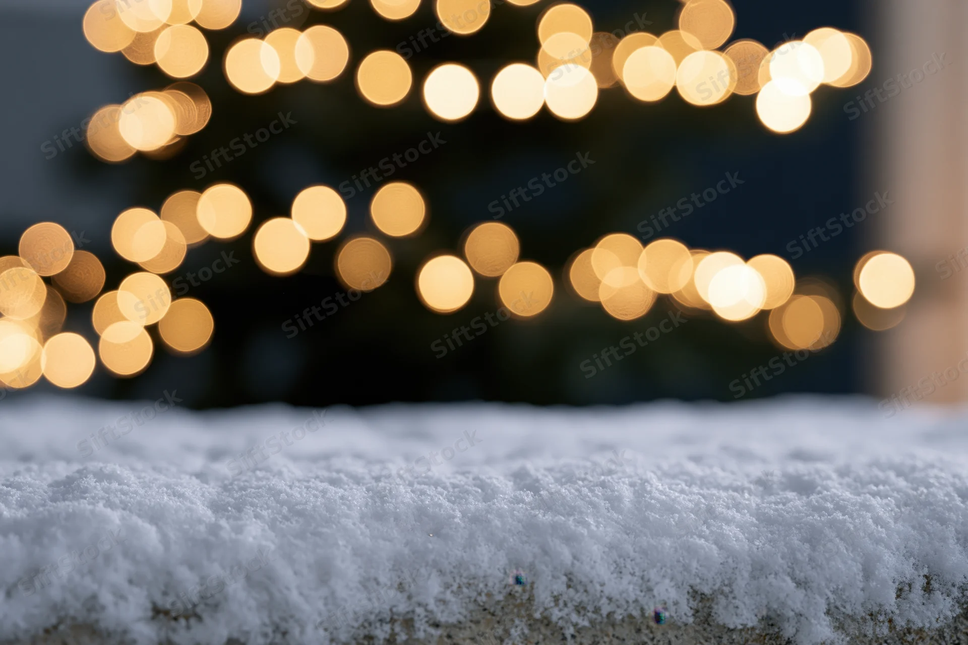 Snow-covered surface in foreground with blurred christmas lights in background