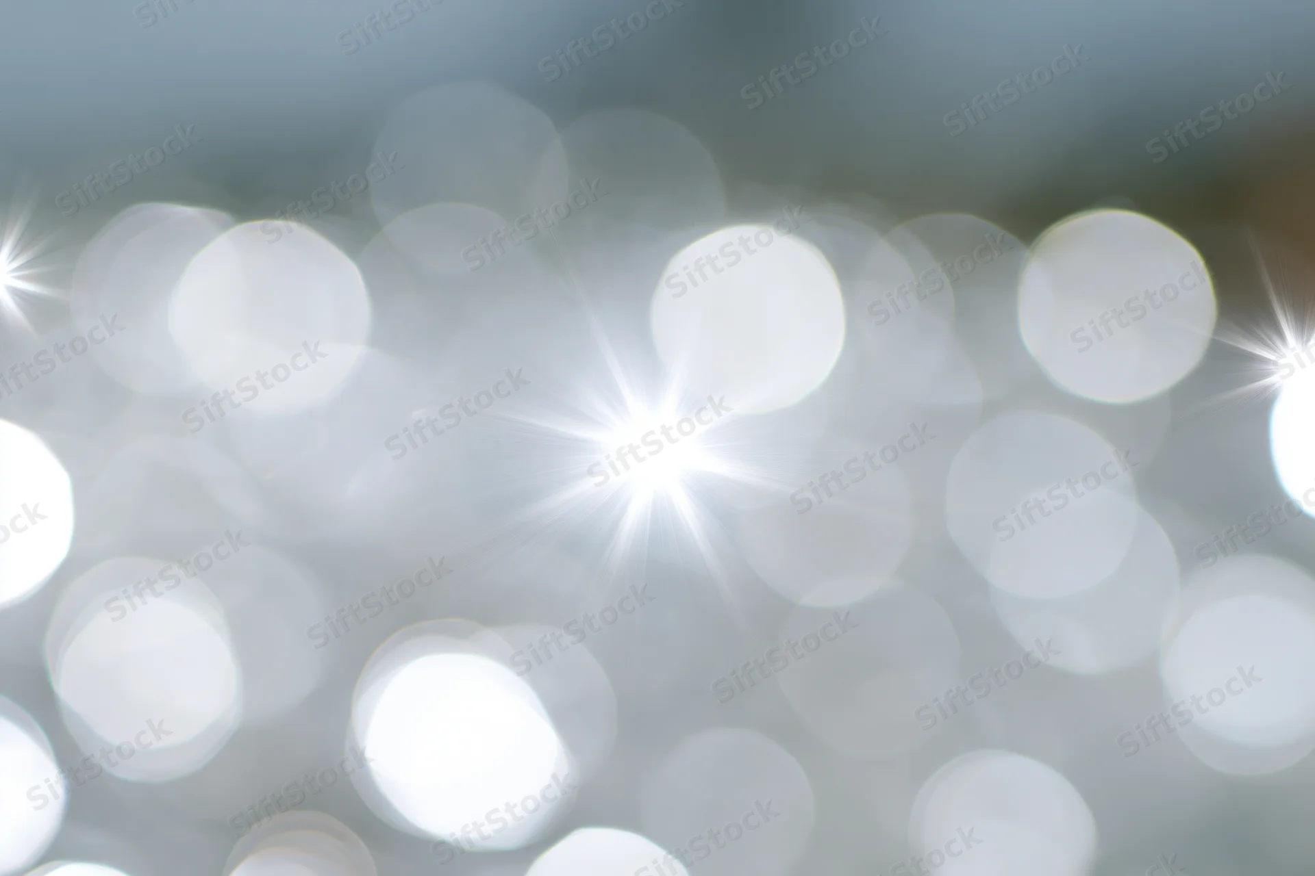 Soft abstract background of out-of-focus white and pale silver bokeh lights with starburst highlights