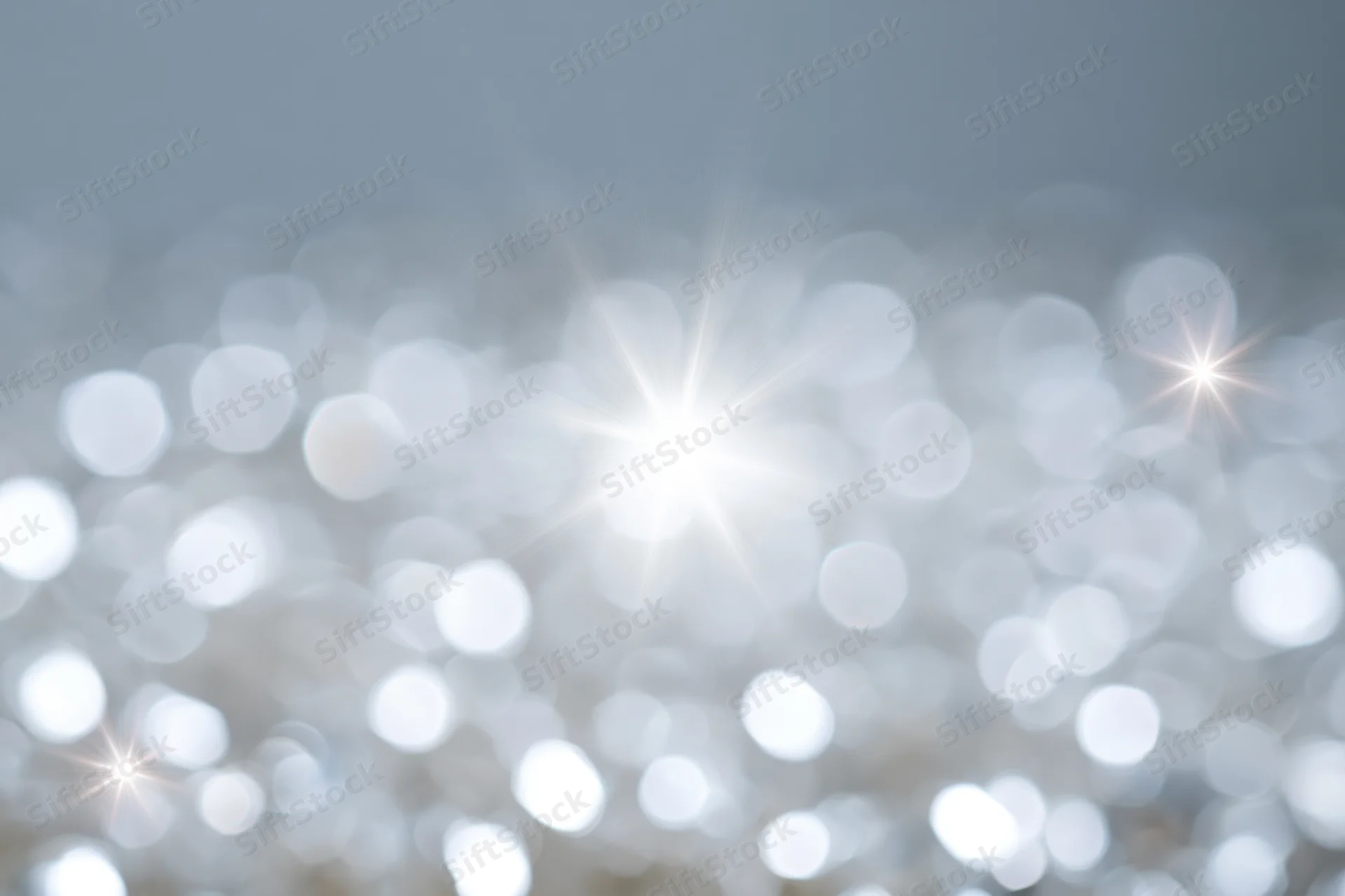 Soft abstract background of out-of-focus white and pale silver lights with starburst highlights