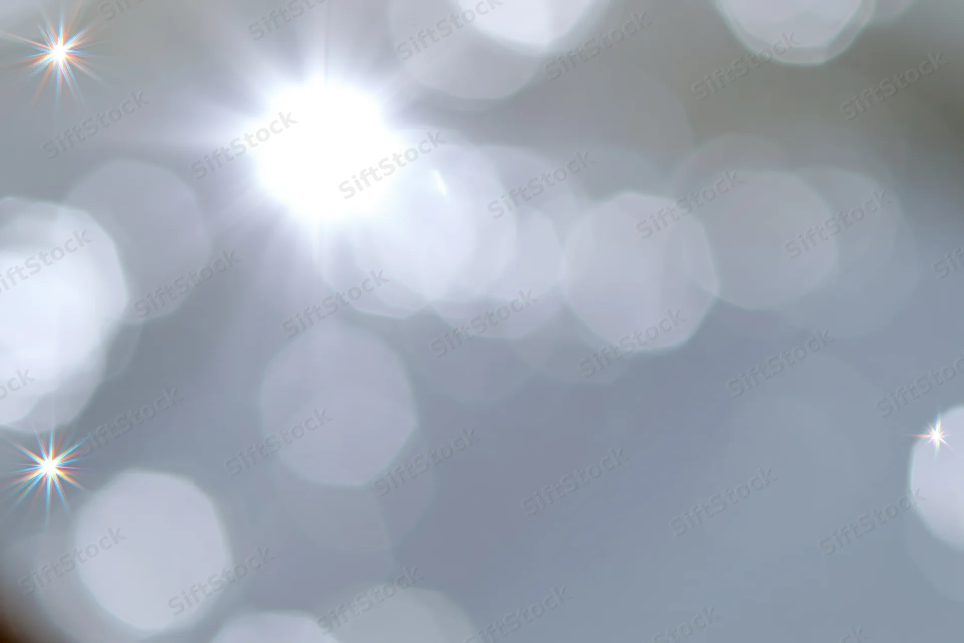 Soft abstract background of out-of-focus white and pale silver bokeh lights with starbursts and glow