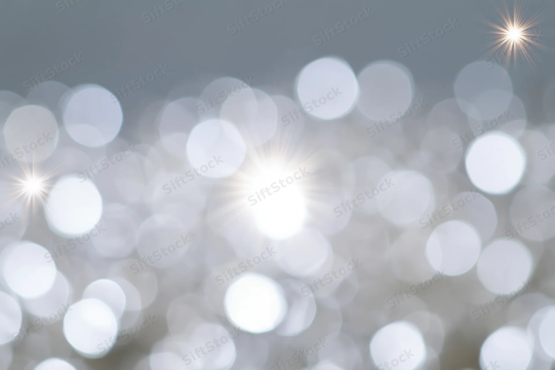Soft abstract background of out-of-focus white and pale silver bokeh lights with starburst flares