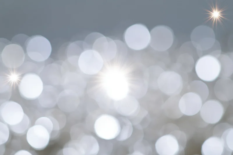 Soft abstract background of out-of-focus white and pale silver bokeh lights with starburst flares