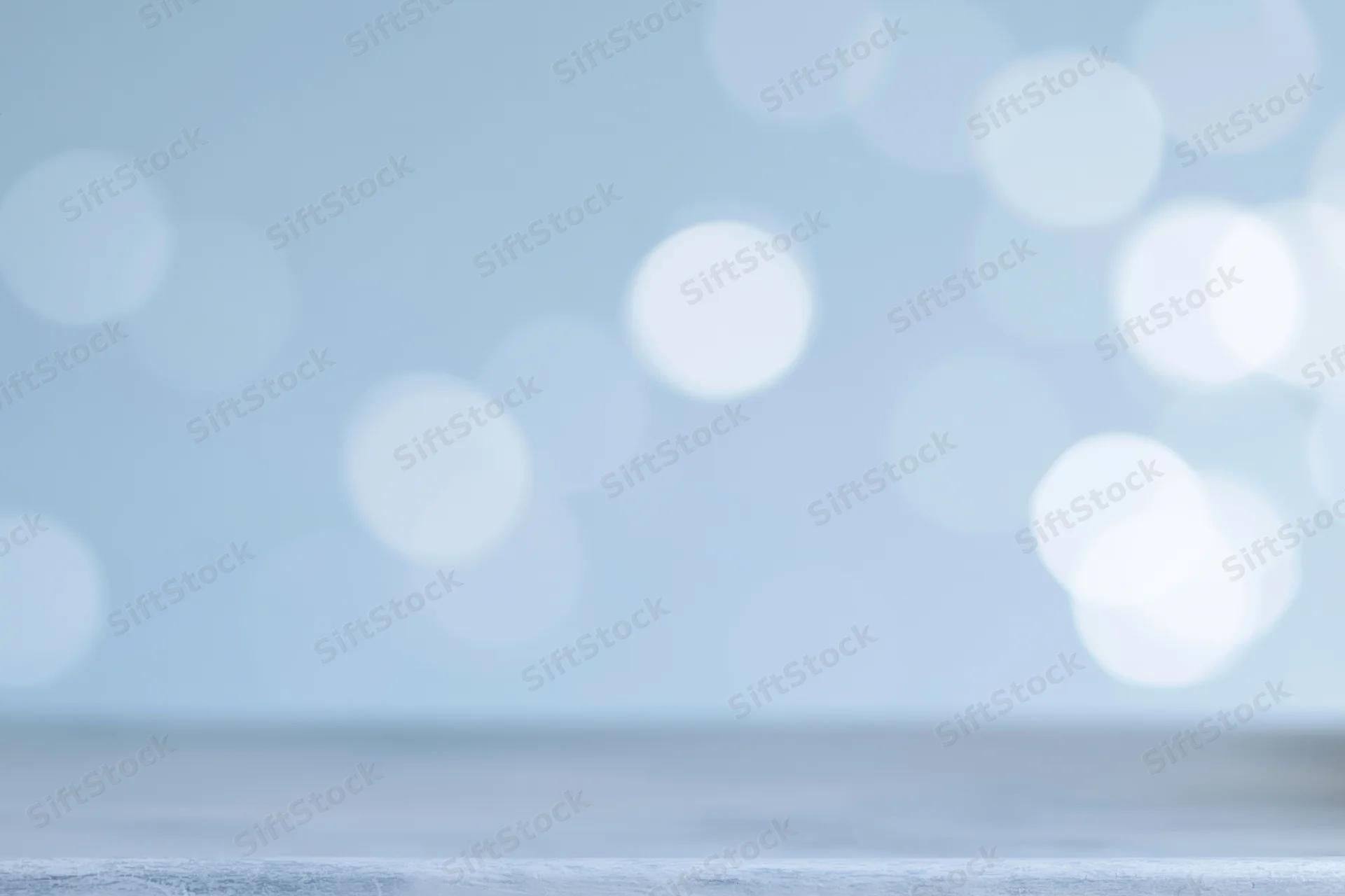 Soft defocused bokeh circles in pastel blue and white forming an abstract background with copyspace at the bottom