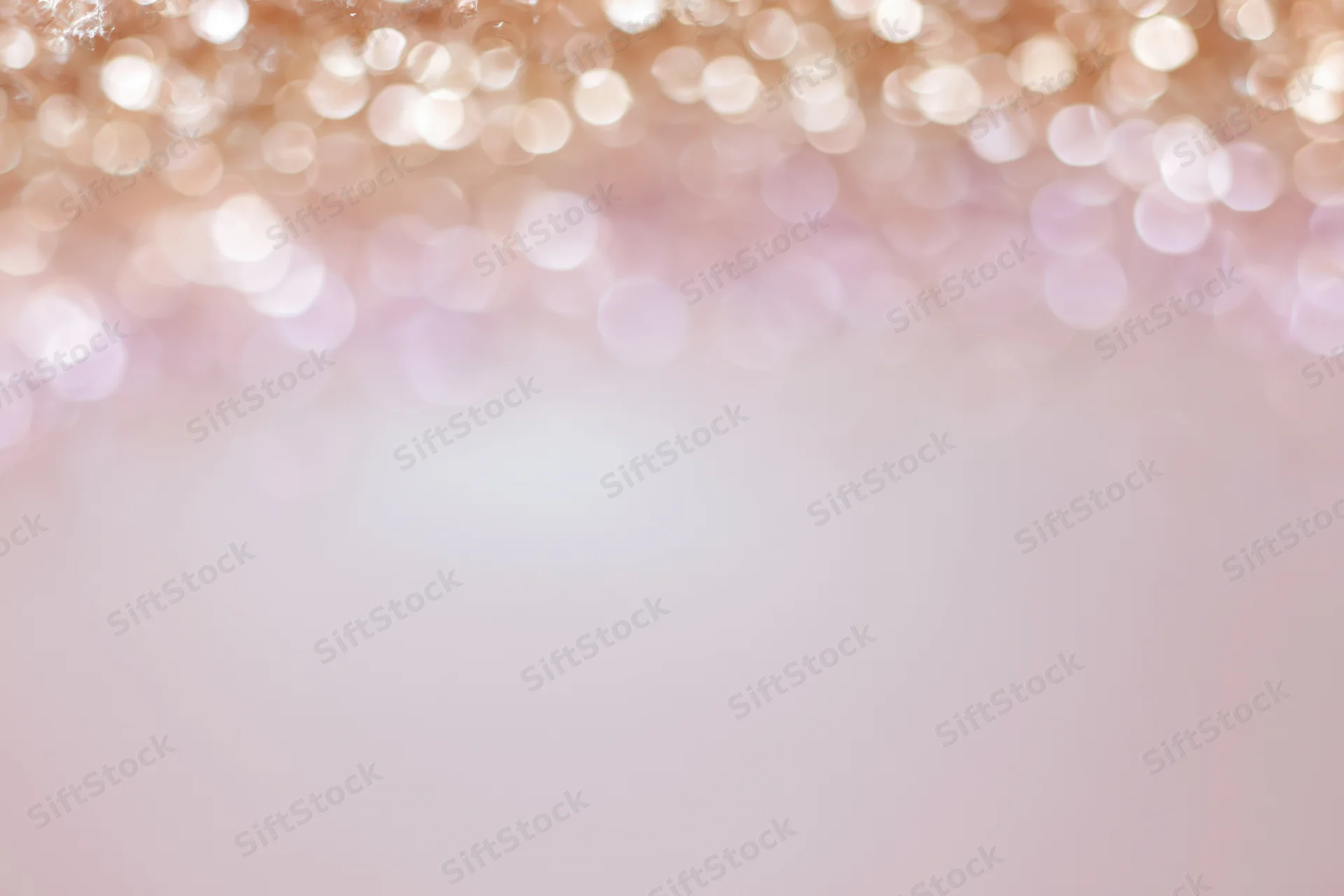 Soft abstract bokeh background with out-of-focus light orbs in pastel pink and gold tones, creating a festive glow