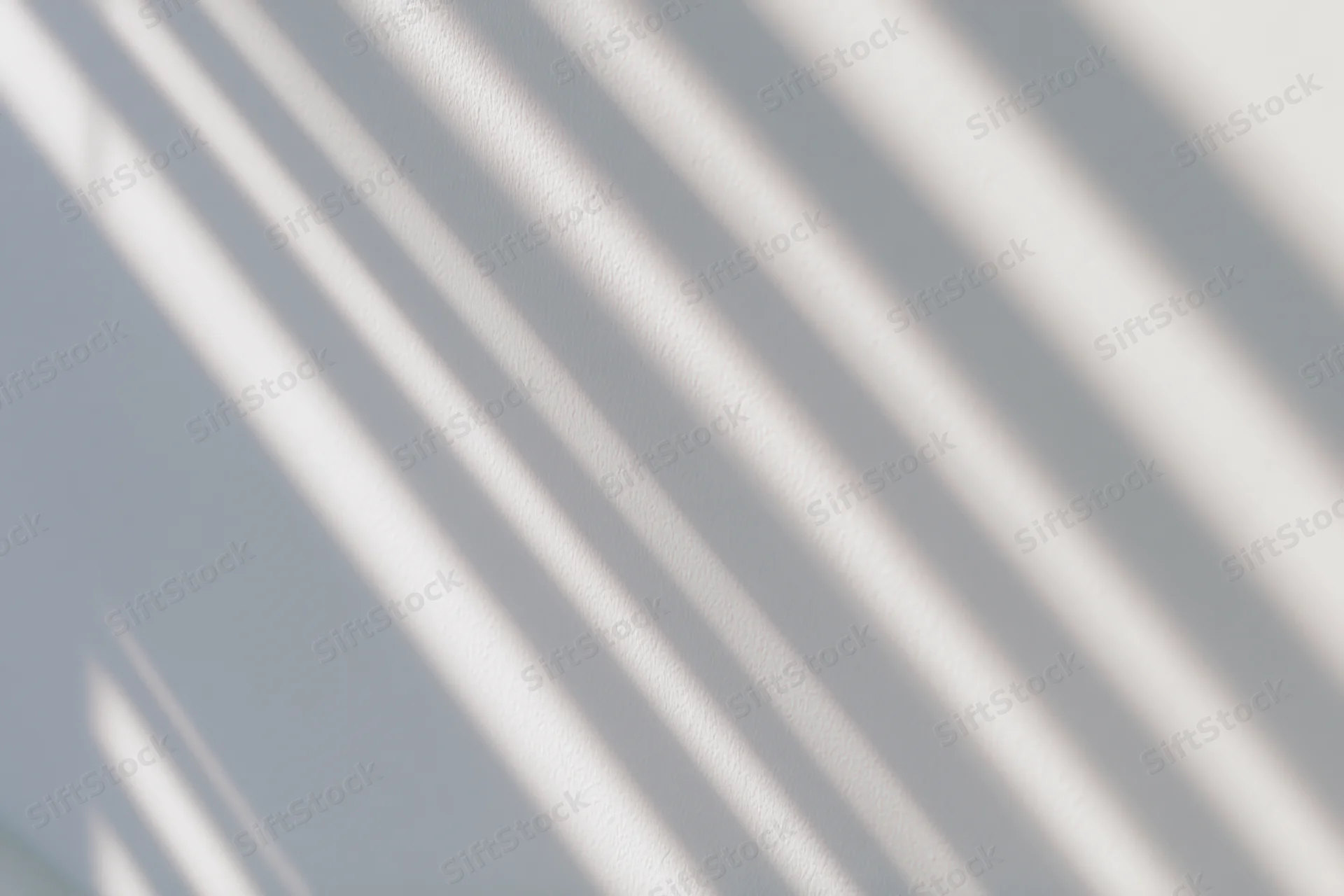 Diagonal shadows from window blinds cast across a white wall in a bright interior