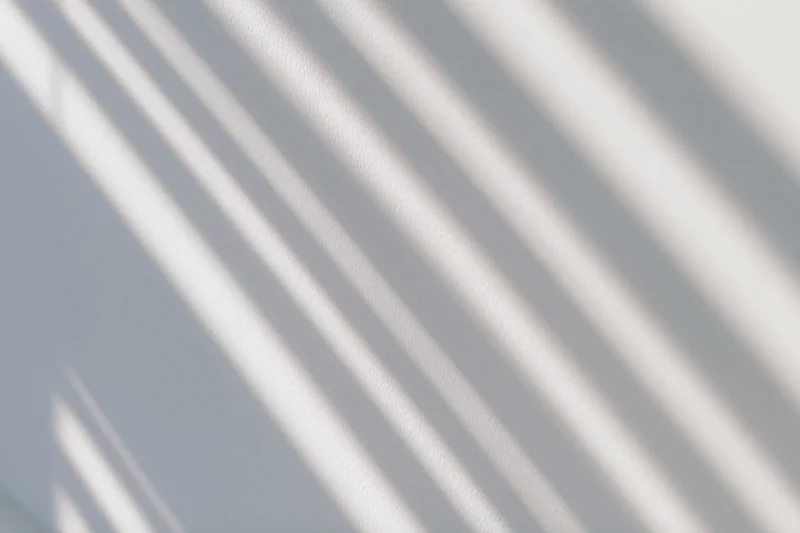 Diagonal shadows from window blinds cast across a white wall in a bright interior