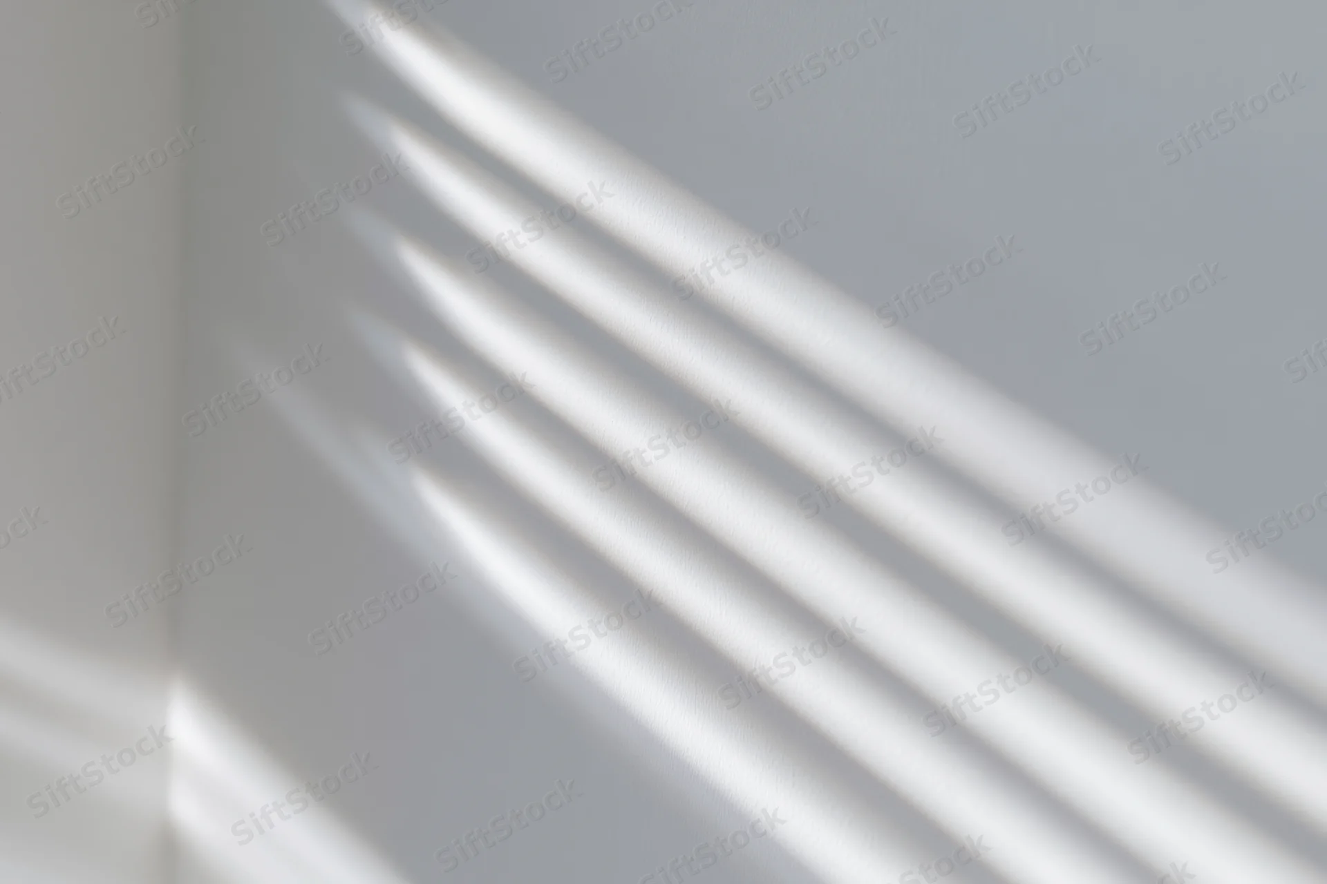 Diagonal shadows from window blinds cast across a white interior wall