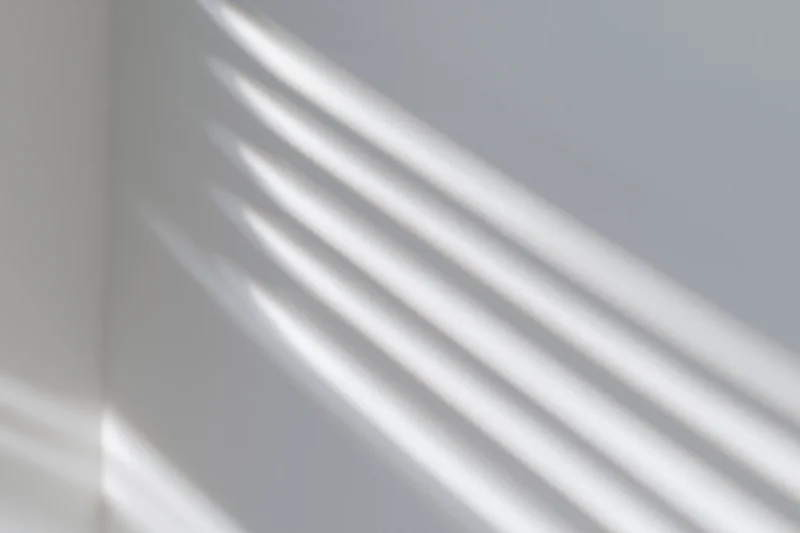 Diagonal shadows from window blinds cast across a white interior wall