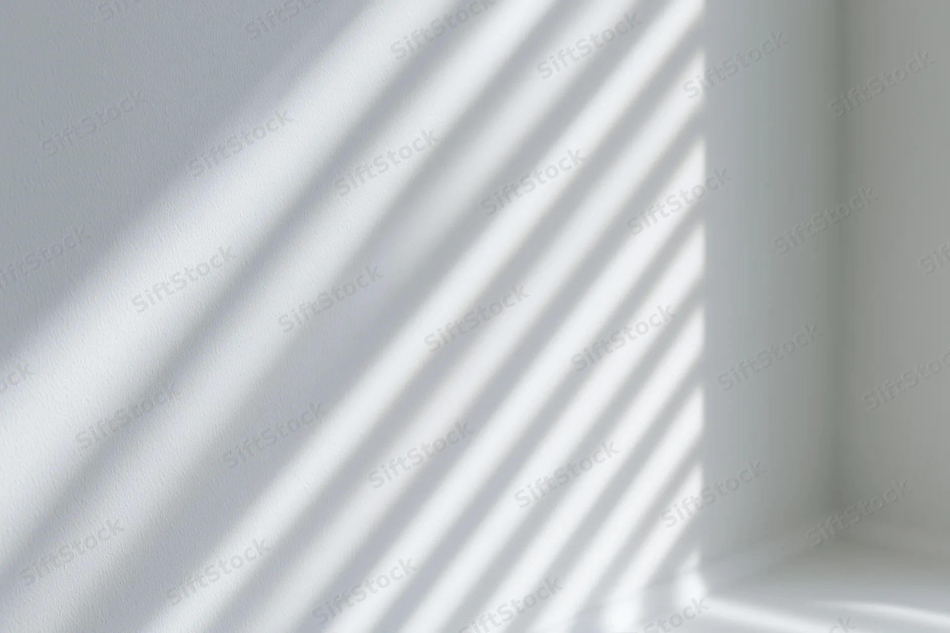 Diagonal shadows from window blinds cast across a white interior wall corner