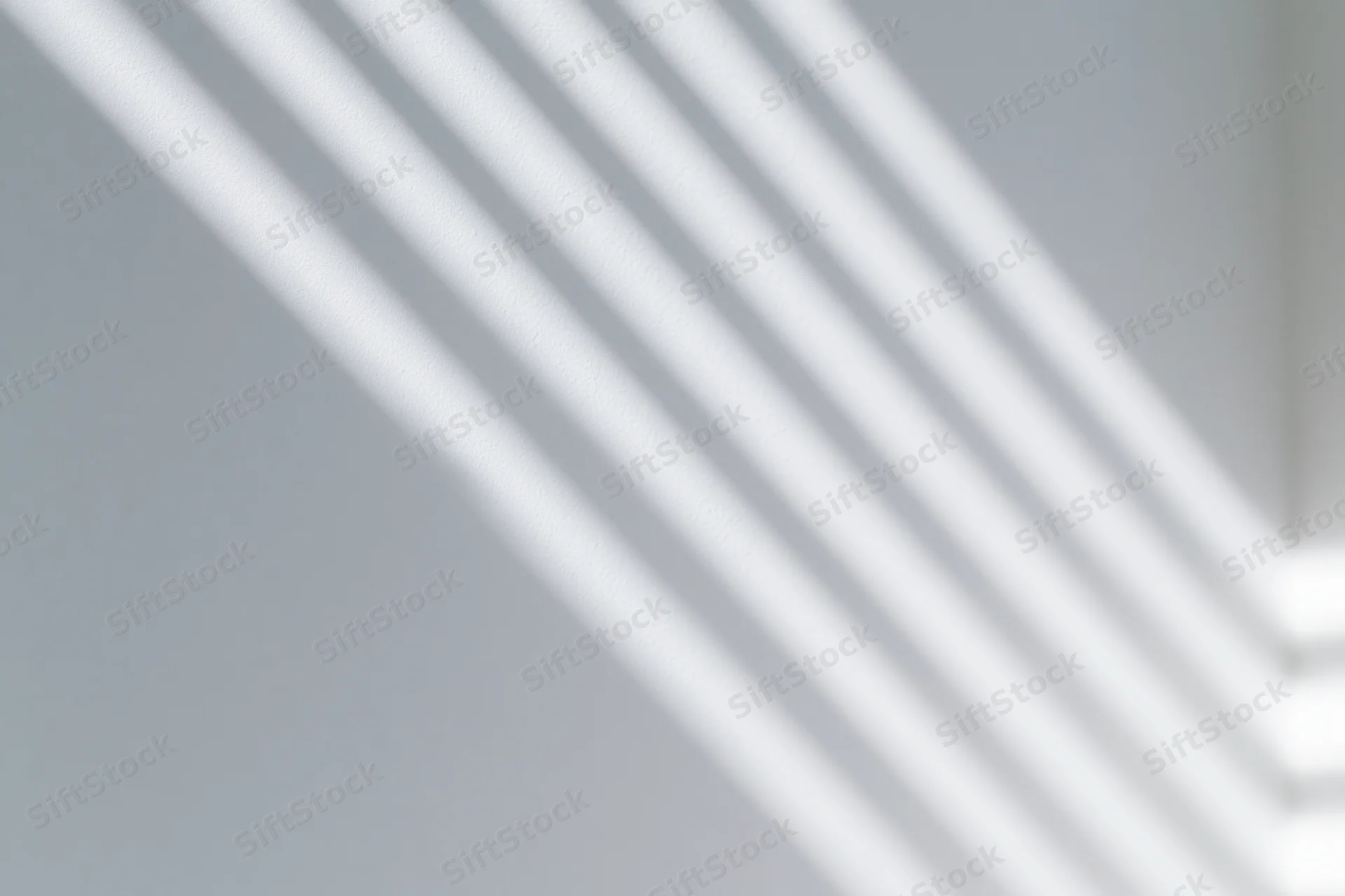 Diagonal shadows from window blinds cast across a white wall in an interior space