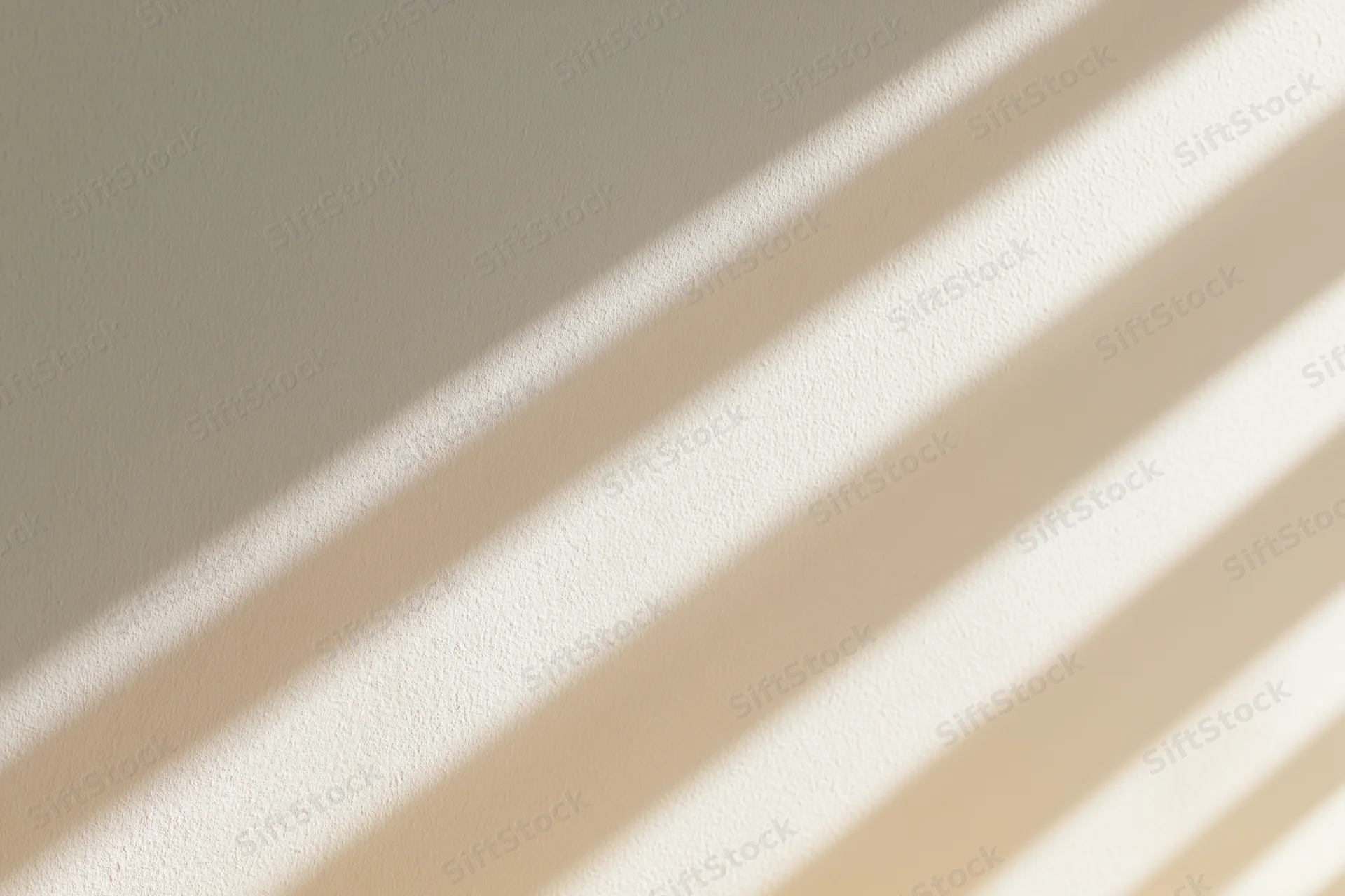 Diagonal window light shadows cast across a plain warm wall interior