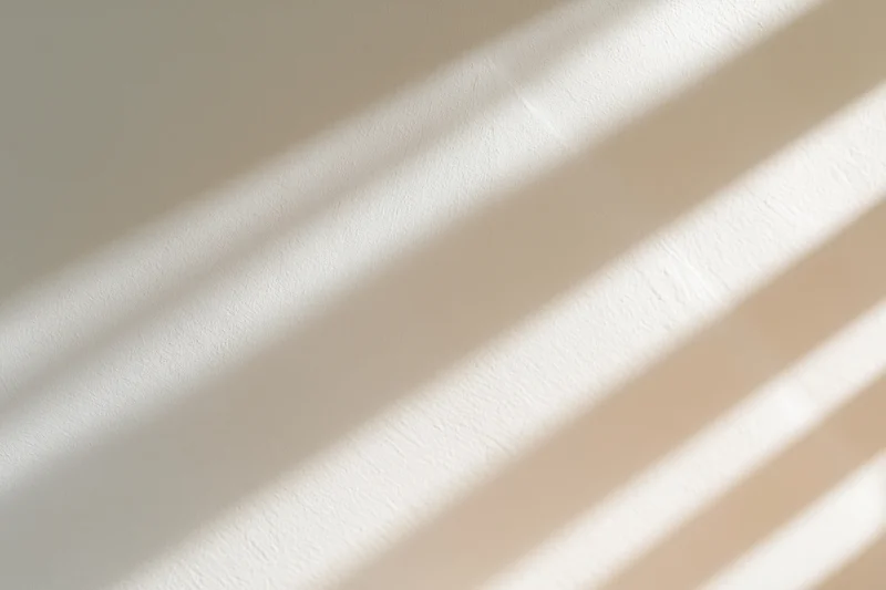 Diagonal window light shadows cast across a plain warm wall in an interior space