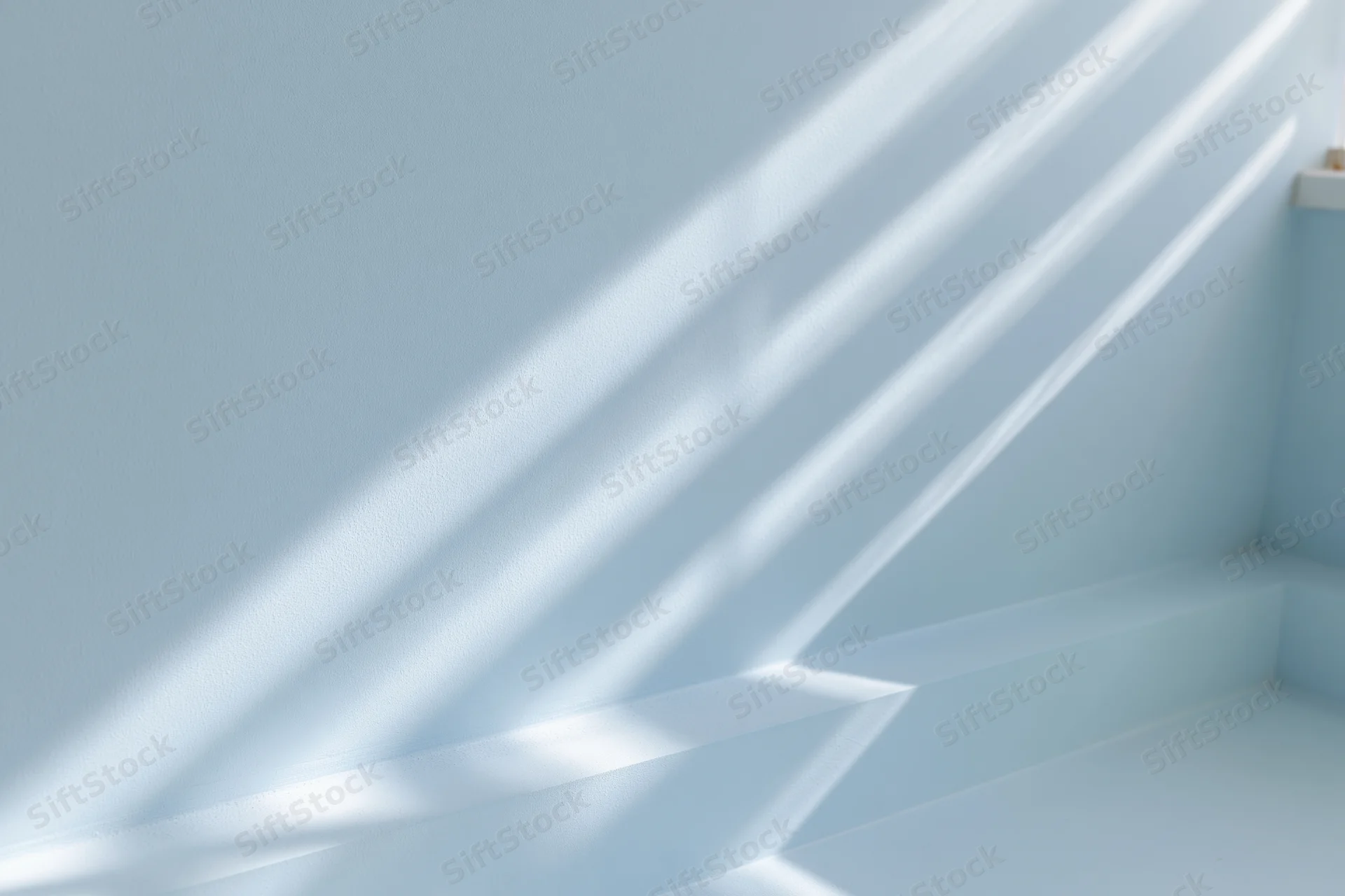 Diagonal sunlight and shadows cast across a light blue interior wall and floor corner