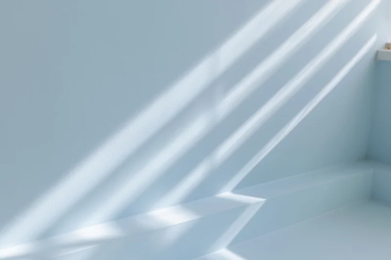 Diagonal sunlight and shadows cast across a light blue interior wall and floor corner
