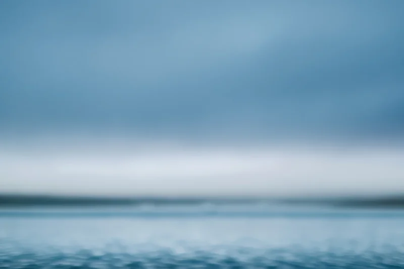 Soft blurred gradient of blue sky and water with indistinct horizon line