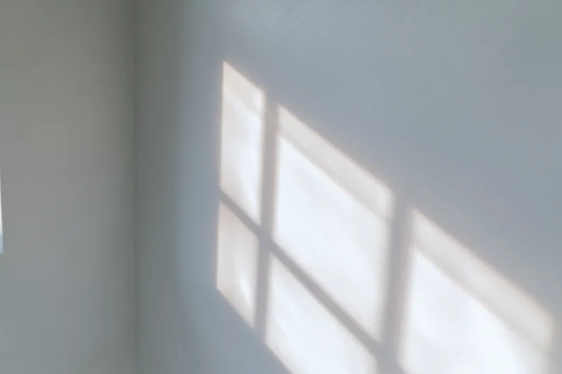 Soft grid shadow from a window cast across a plain white interior wall