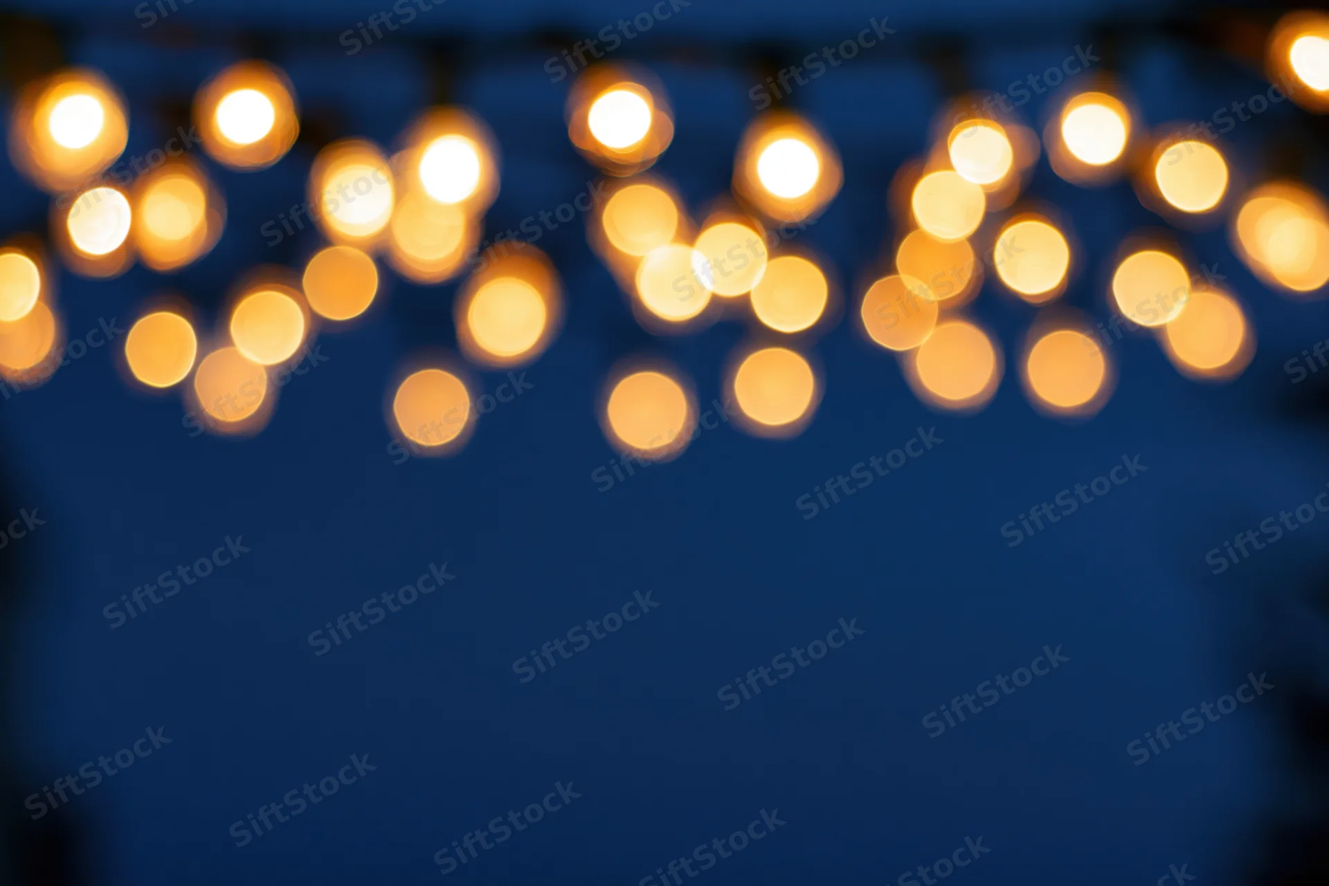 String lights hanging out of frame at the top creating a blurred bokeh effect against a dark blue background with copyspace below