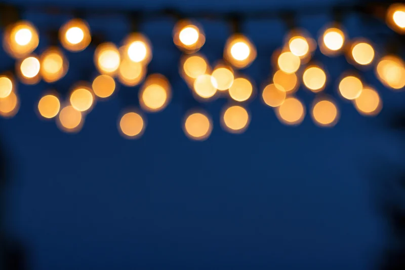 String lights hanging out of frame at the top creating a blurred bokeh effect against a dark blue background with copyspace below