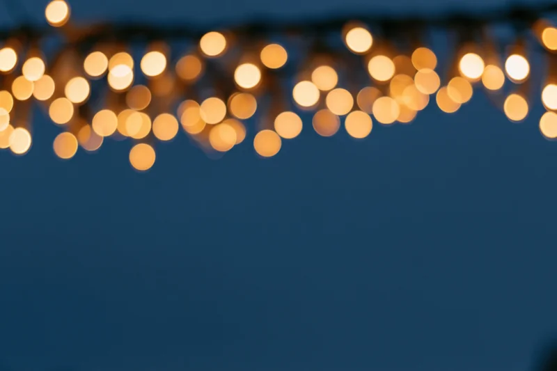 String lights hanging out of frame at the top, blurred with warm bokeh glow against dark blue background, creating copyspace below