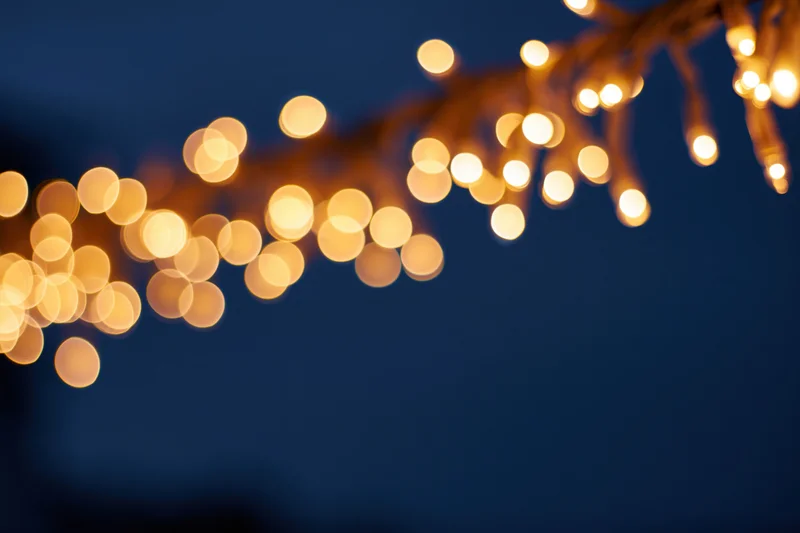 String lights hanging diagonally across the top of the frame against a dark blue background with bokeh effect and copyspace below