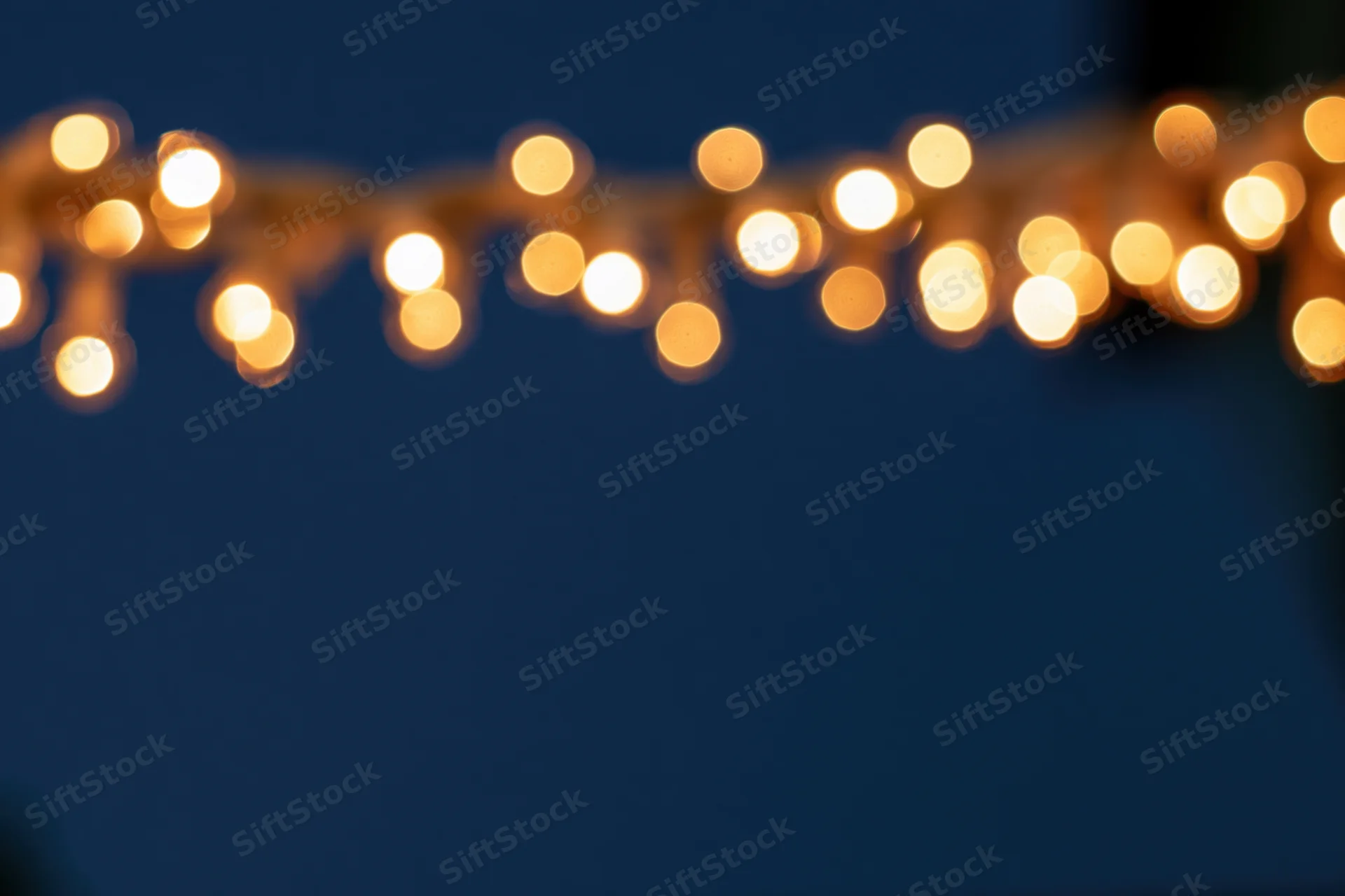 String lights glowing softly out of focus at the top of the frame against a dark blue background with copyspace below