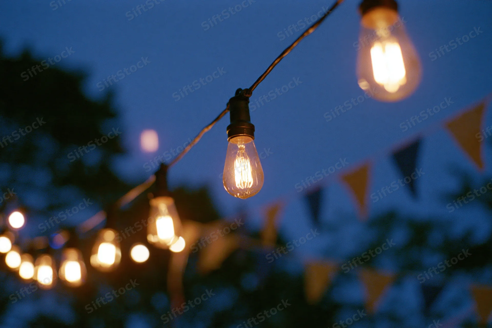 String of warm edison bulbs hanging outdoors at twilight with bunting flags in the background